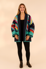 Colorful quilted open-front jacket with geometric rainbow patterns, green diamond quilted panels, and relaxed oversized cut, styled with slim-fit jeans and black ankle boots.