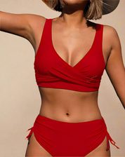 Bold red bikini set featuring a wrap-front top with wide straps and a deep neckline, paired with high-waisted ruched bottoms that tie at the sides. The fabric has a smooth matte finish with solid, uniform color throughout, showcasing a modern and supportive design.