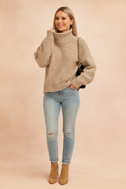 Beige chunky knit turtleneck sweater with textured pattern, paired with light blue distressed skinny jeans, tan ankle boots, and a black shoulder bag with gold chain strap.