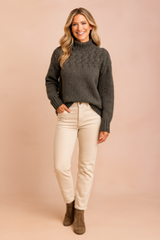 Charcoal chunky knit turtleneck sweater with intricate braided detail across the chest, paired with high-waisted cream jeans and taupe suede ankle boots.