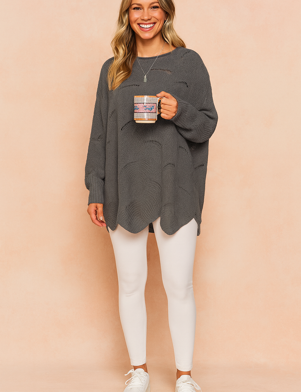Oversized charcoal grey knit sweater with subtle horizontal distressed holes, long sleeves, and curved hemline, paired with white fitted leggings and white lace-up sneakers.