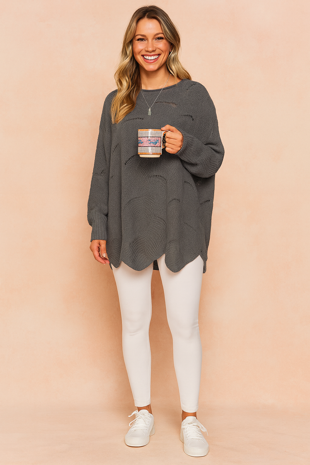 Oversized charcoal grey knit sweater with subtle horizontal distressed holes, long sleeves, and curved hemline, paired with white fitted leggings and white lace-up sneakers.