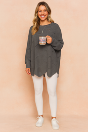 Oversized charcoal grey knit sweater with subtle horizontal distressed holes, long sleeves, and curved hemline, paired with white fitted leggings and white lace-up sneakers.