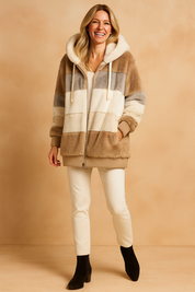Color-blocked faux fur hooded coat in taupe, cream, and light gray stripes, paired with slim white pants and black ankle boots.
