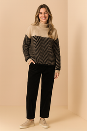 Two-tone turtleneck sweater with beige upper panel and black-and-beige herringbone patterned lower section, paired with black wide-leg trousers and beige suede loafers.