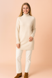 Cream beige ribbed high-neck sweater with long sleeves, finely knitted texture, and extended ribbed cuffs, styled over straight white trousers and paired with brown suede ankle boots.