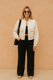 Cream cropped button-up jacket with front pockets, styled over a black top and black high-waisted trousers, paired with beige shoes and sunglasses.