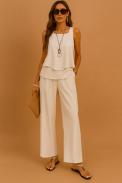 Elegant two-piece cream co-ord set featuring a sleeveless layered tank top and wide-leg trousers, accessorized with black sandals and a tan woven clutch.
