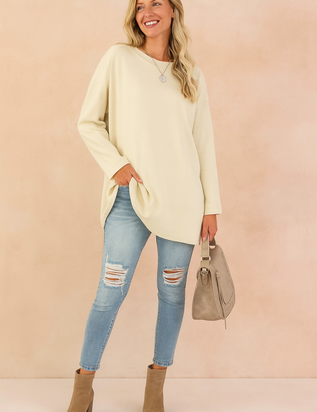 Oversized cream long-sleeve tunic paired with light blue distressed skinny jeans, taupe ankle boots, and a matching taupe handbag.