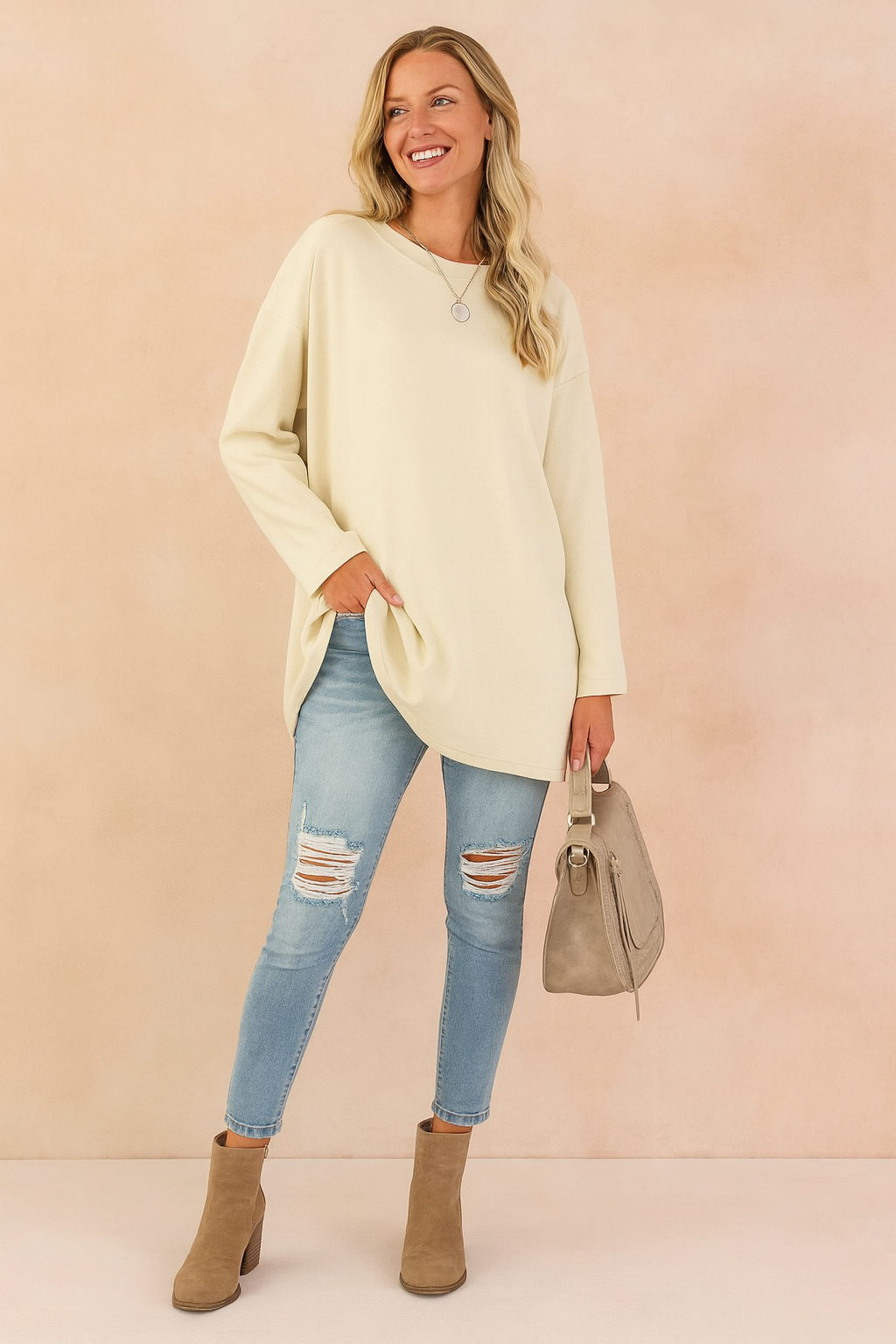Oversized cream long-sleeve tunic paired with light blue distressed skinny jeans, taupe ankle boots, and a matching taupe handbag.