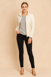 Cream puffer jacket with horizontal quilted design, styled over a black and white striped top and slim black jeans.