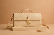Cream woven leather handbag with gold key clasp, top handle, and crossbody strap, displayed on a matching pastel platform.