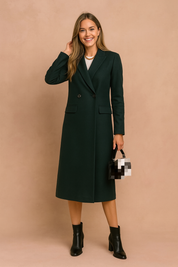 Elegant long dark green wool coat with double-breasted button closure, notched lapel collar, flap pockets, and a sleek tailored silhouette, paired with black ankle boots and a structured handbag.
