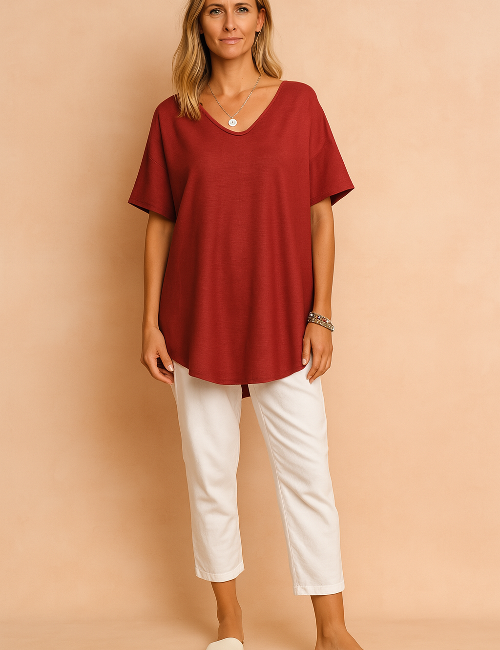 Elegant deep red short-sleeve tunic blouse made from lightly textured fabric, featuring a relaxed drape and a scoop neckline, paired with crisp white ankle-length trousers and minimal slide sandals—perfect for effortless casual chic.