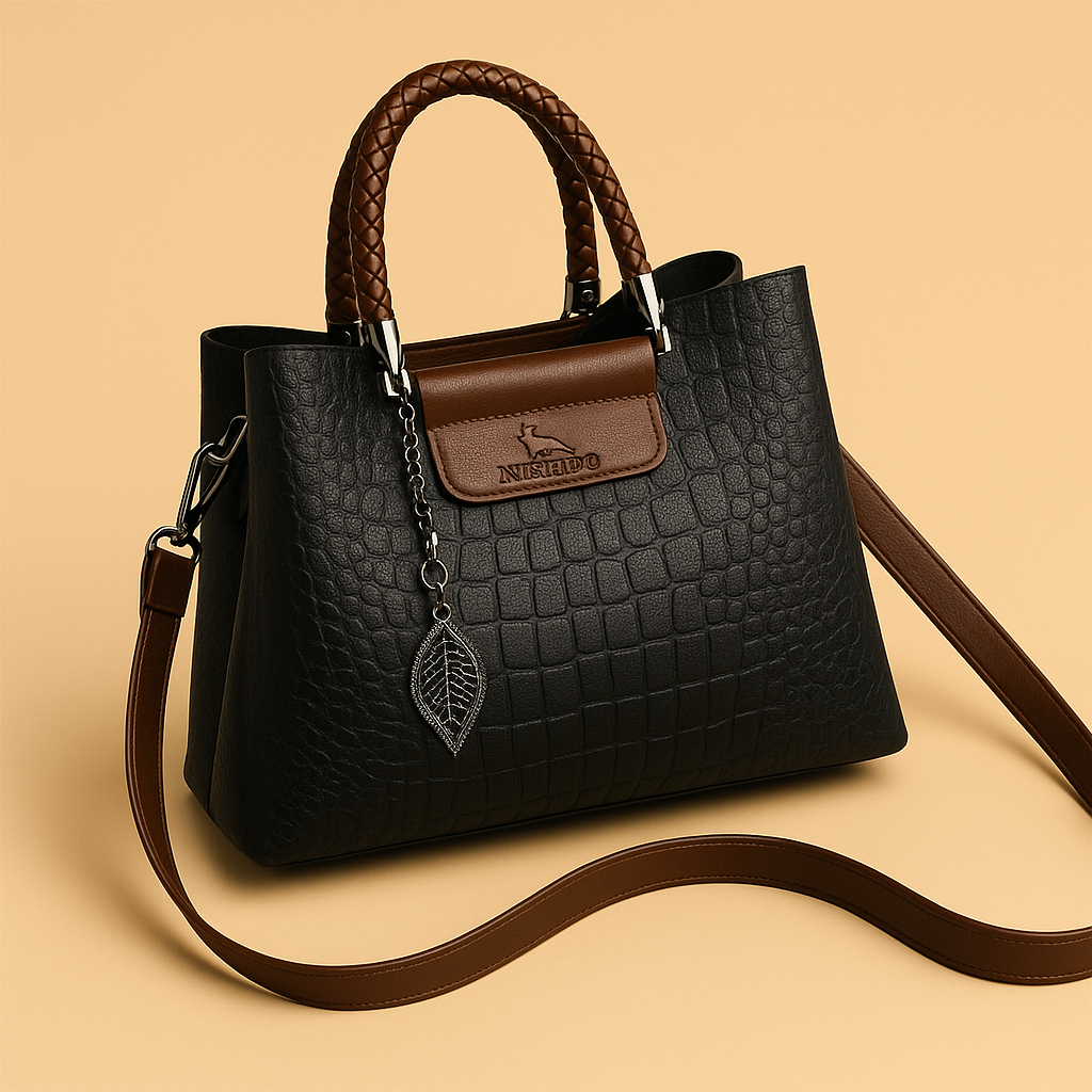 Black crocodile-embossed handbag with brown braided handles and detachable strap, silver hardware, and leaf pendant charm on a soft beige background.