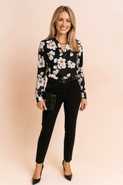 Black floral blouse with long sleeves featuring soft pink and white blossoms, paired with slim-fit black trousers, a black leather clutch with a gold accent, and black pointed-toe heels.
