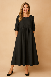Black linen A-line maxi dress with elbow-length sleeves, a gathered high waist, discreet side pockets, and a wide flowing hem.