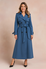Double-breasted long blue trench coat with wide lapels, waist belt, side pockets, and black button detailing, paired with black pointed-toe high heels.