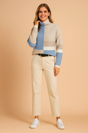 Color-block turtleneck sweater in beige, sky blue, and taupe with ribbed knit texture, paired with cream straight-leg trousers, black belt, and white sneakers.