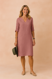 Minimalist V-neck shift dress in dusty rose with 3/4 rolled sleeves and clean silhouette, styled with subtle accessories and flats for a relaxed yet elegant look.