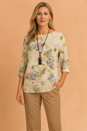Loose-fit floral blouse with three-quarter sleeves and a soft watercolor-style print in yellow, green, pink, and blue tones, styled with beige trousers for a fresh casual look.