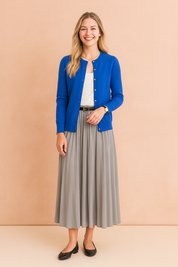 Elegant royal blue button-up cardigan paired with a white top and flowing grey pleated midi skirt, styled with a black belt and classic black ballet flats.