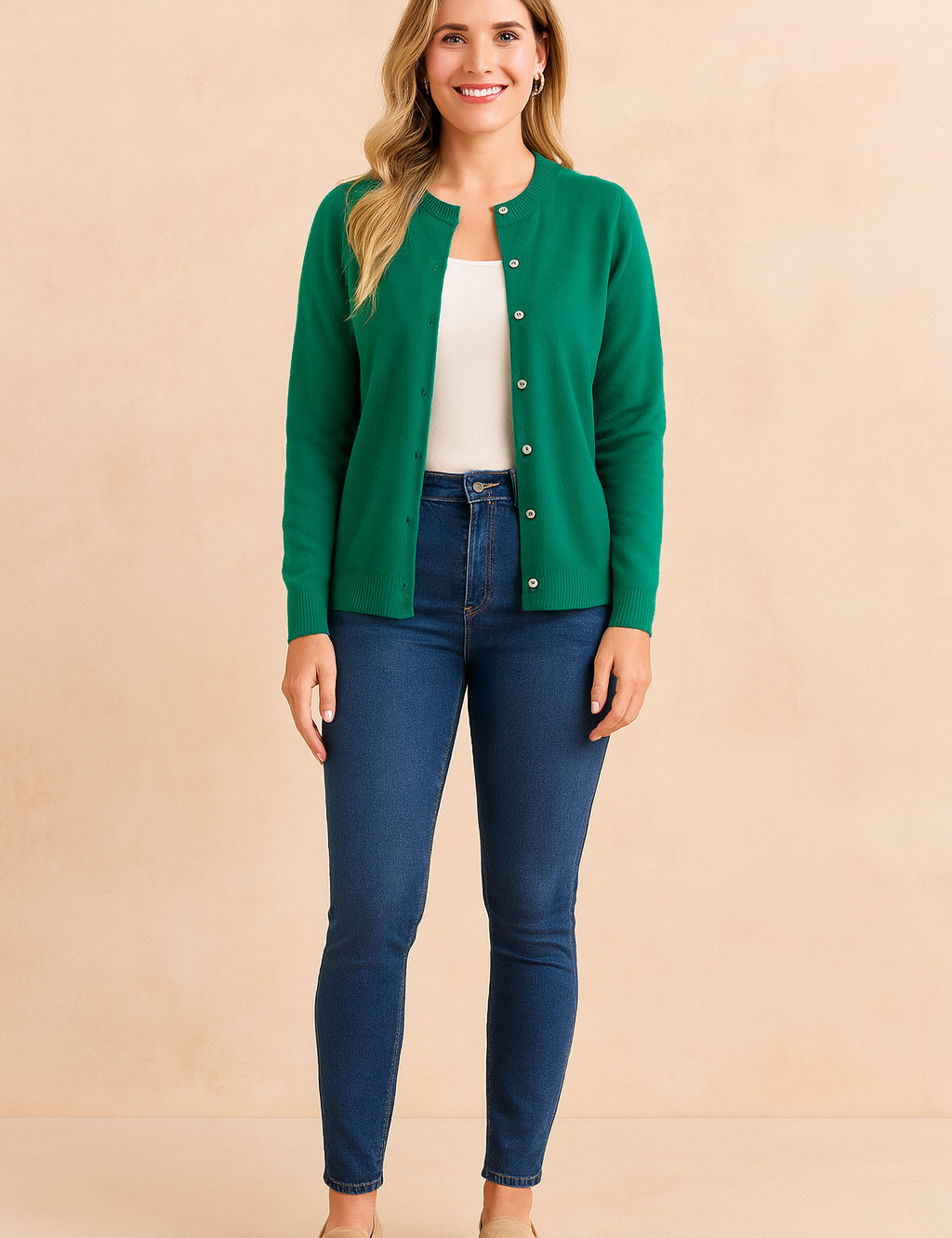 Emerald green button-front cardigan layered over a white tank top, paired with dark blue skinny jeans and beige suede loafers.