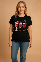 Black short-sleeve graphic tee featuring three red wine glasses with festive Christmas-themed decorations including a Santa hat, reindeer antlers, and holiday lights, printed in vivid colors on a snow-sprinkled background.