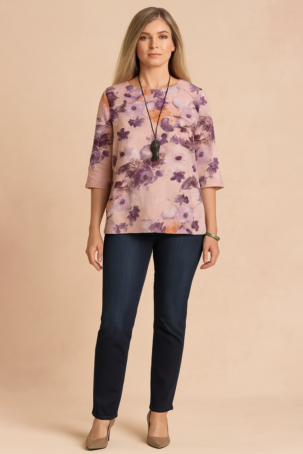 Loose-fit floral blouse with watercolor-effect purple and orange flower motifs on a pale pink base, featuring 3/4 sleeves and a straight hem, styled with dark jeans and taupe heels.