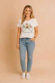 White short-sleeve t-shirt featuring a playful envelope floral print, paired with classic high-rise blue jeans and white sneakers.