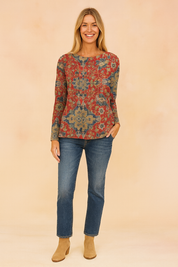 Long-sleeve sweater with an intricate red, blue, and beige floral tapestry pattern, paired with classic blue jeans and tan suede ankle boots.