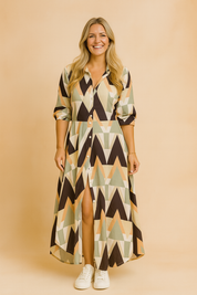 Geometric print maxi shirt dress with collar, button-down front, front slit, and three-quarter sleeves in a bold pattern of black, peach, sage, and off-white triangles, styled with white sneakers.
