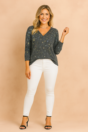 Dazzling black V-neck sequin blouse with long sleeves, featuring a multicolored sparkle effect and a relaxed fit, paired with sleek white skinny trousers.