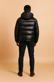 Back view of a glossy black puffer jacket with hood, horizontal quilted padding, and casual modern fit.