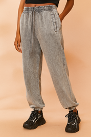 High-waisted gray acid-washed sweatpants with elastic waistband, drawstring tie, side slit pockets, and elasticized cuffs, styled with black chunky sneakers featuring bold white details.