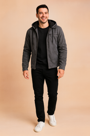 Gray hooded jacket with black fleece lining, front zipper, and drawstring details, paired with black trousers and white sneakers.