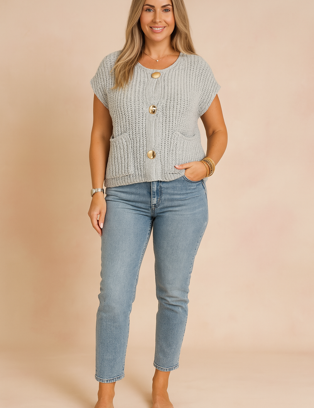 Black knit sleeveless button-front blouse with large gold buttons, styled with light-wash high-rise jeans and nude heeled sandals, photographed in a soft pastel fashion studio background