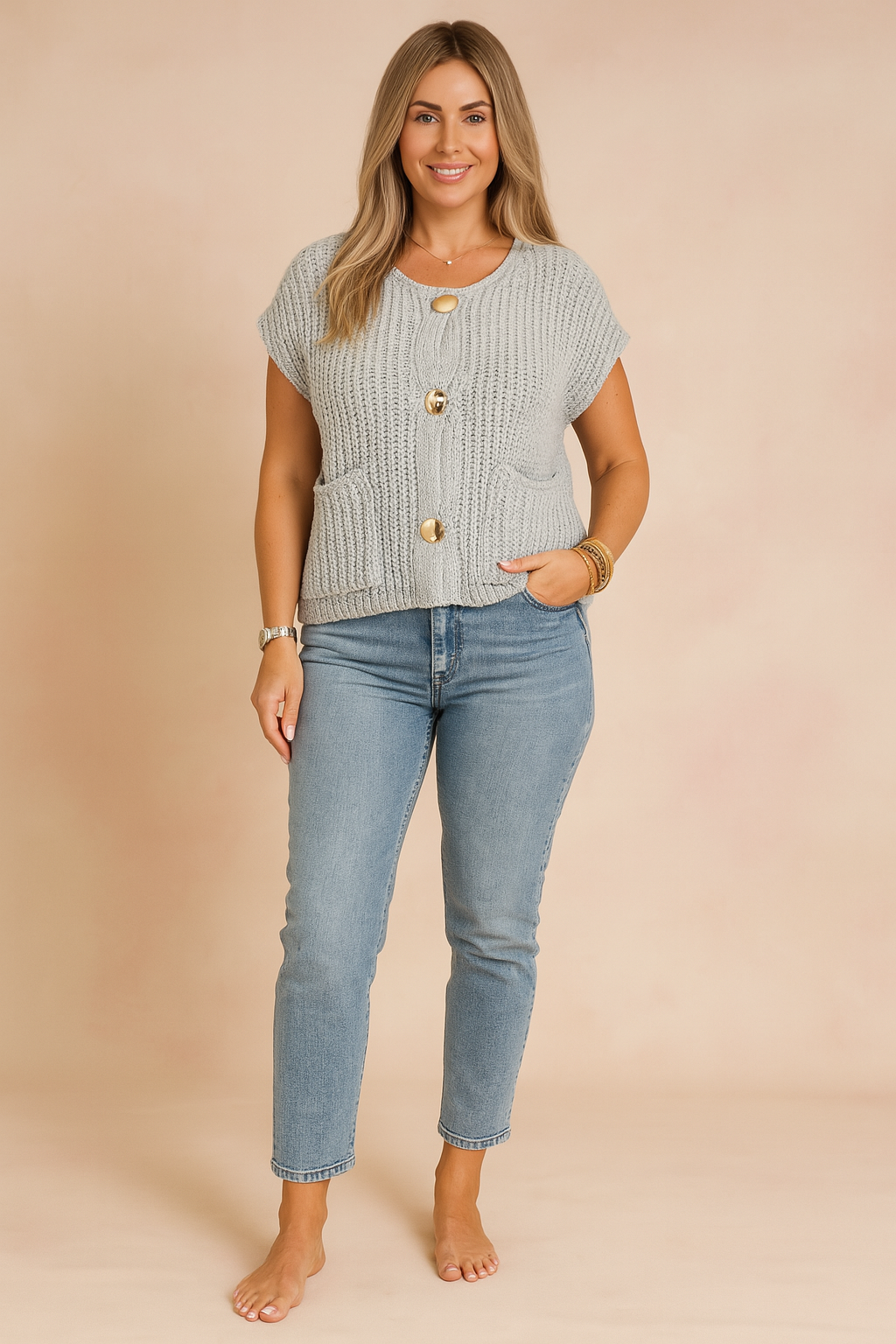 Black knit sleeveless button-front blouse with large gold buttons, styled with light-wash high-rise jeans and nude heeled sandals, photographed in a soft pastel fashion studio background