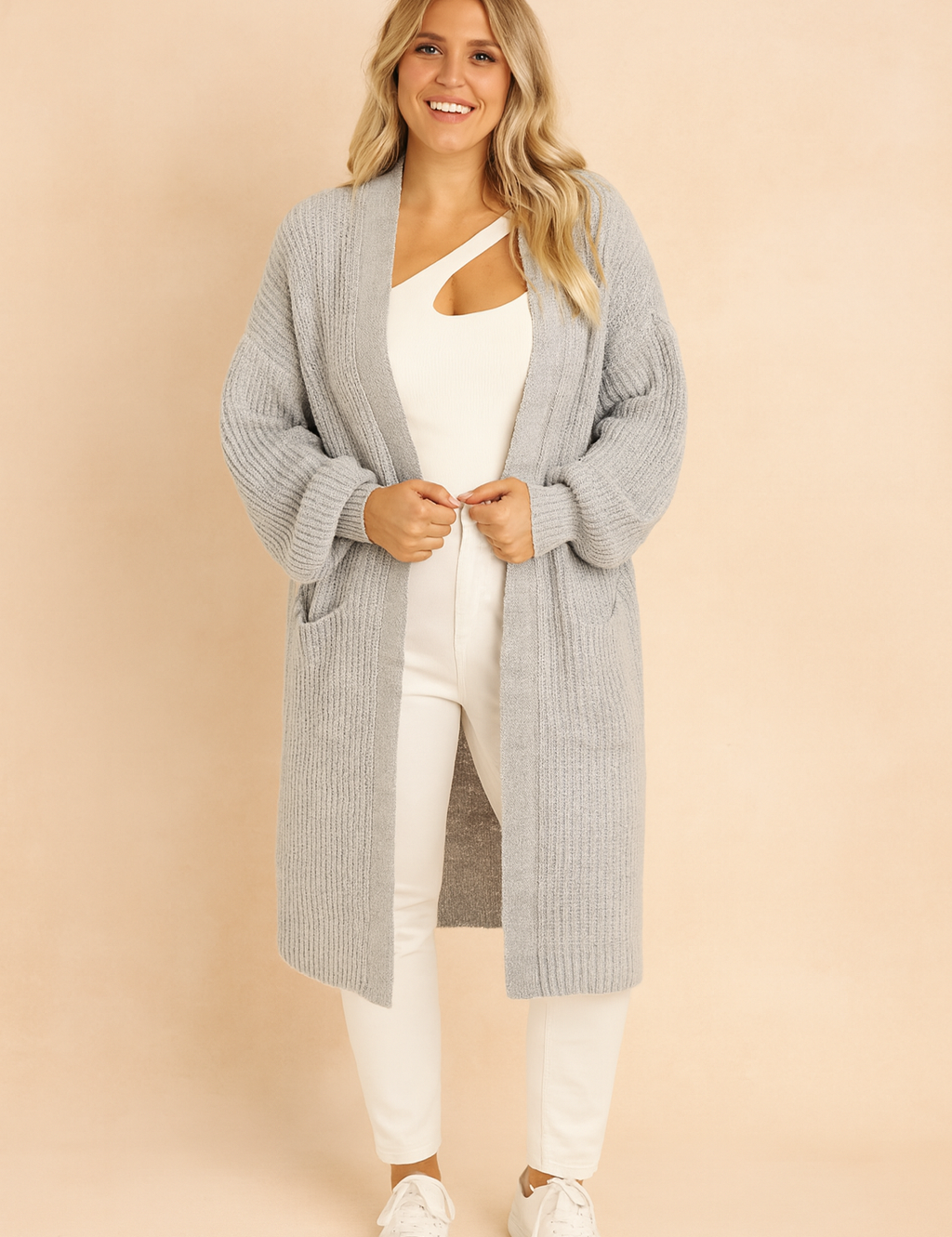 Light gray oversized ribbed knit cardigan with dropped shoulders, long sleeves, and open front, styled over a white cut-out top, white slim-fit pants, and white sneakers.