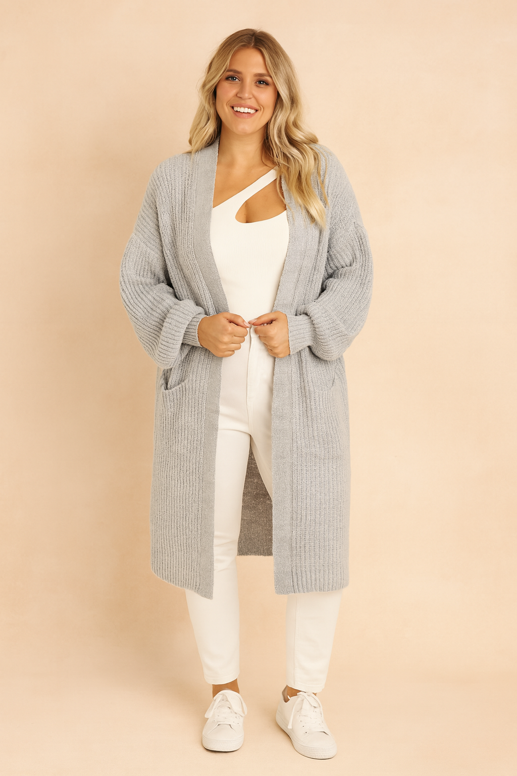 Light gray oversized ribbed knit cardigan with dropped shoulders, long sleeves, and open front, styled over a white cut-out top, white slim-fit pants, and white sneakers.