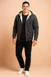 Charcoal gray zip-up hoodie with cream sherpa fleece lining, drawstring hood, and ribbed cuffs, styled with black trousers and white sneakers.