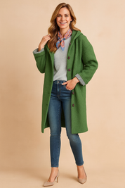 Long green button-up coat with textured fabric, cuff detail, and front pockets styled over a casual top and jeans.