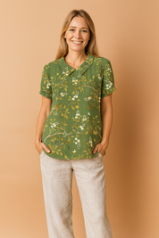 Green linen blouse adorned with a delicate yellow and white floral print, featuring short cuffed sleeves and a classic Peter Pan collar.