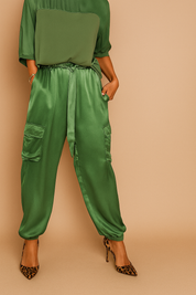 Green satin cargo pants with elastic cuffs, side flap pockets, and a matching fabric tie-waist styled with leopard-print heels.