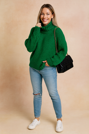 Chunky knit green turtleneck sweater with oversized sleeves, paired with light-wash ripped skinny jeans, white sneakers, and a black quilted chain-strap handbag.