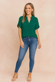 Women's casual outfit featuring a short-sleeve emerald green V-neck blouse paired with high-rise blue skinny jeans.