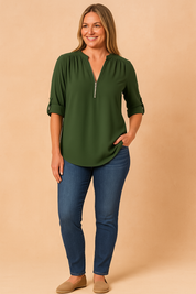 Deep green zip-front blouse with roll-tab sleeves and gentle pleats at the shoulders, paired with classic blue skinny jeans for a clean, everyday look.