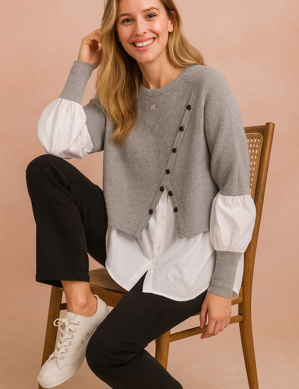 Layered outfit featuring a cropped grey buttoned knit sweater worn over a long white shirt with puff sleeves, paired with straight black trousers and white lace-up sneakers.