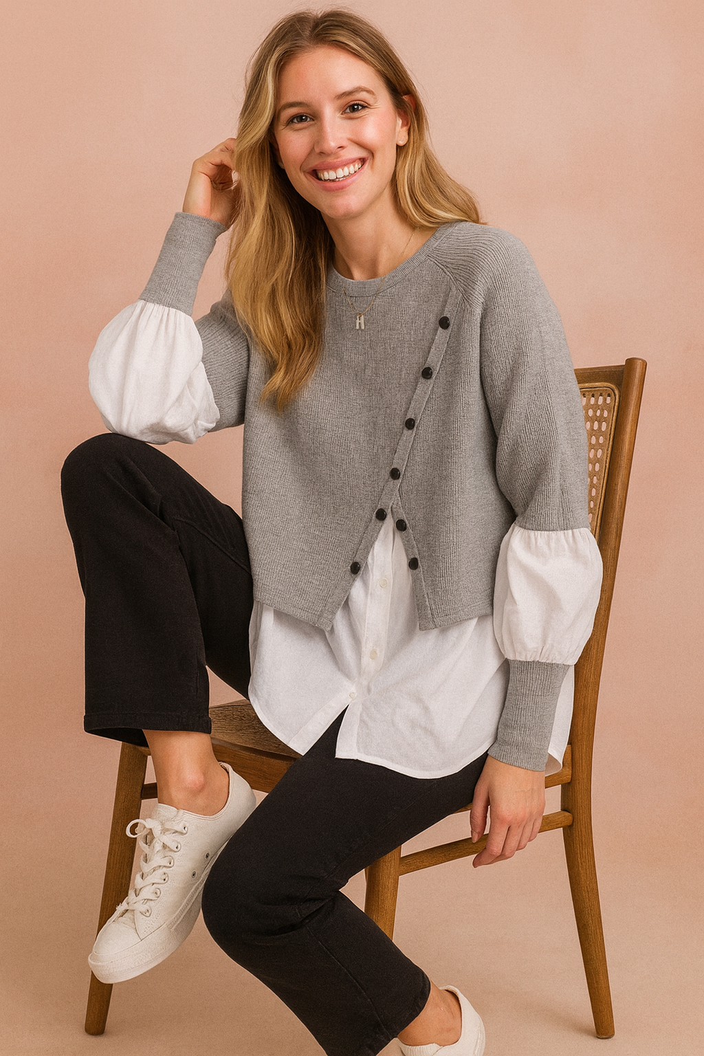 Layered outfit featuring a cropped grey buttoned knit sweater worn over a long white shirt with puff sleeves, paired with straight black trousers and white lace-up sneakers.
