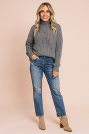 Grey cable-knit turtleneck sweater paired with distressed blue jeans and beige suede ankle boots.